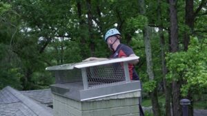 A technician from Owens Chimney Systems inspecting a chimney cap on a roof in Charlotte, NC.