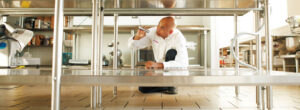 A Franklin Pest Solutions technician inspecting under a stainless steel table in a commercial kitchen in Lafayette, IN.