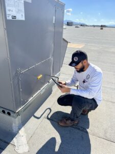 A technician inspecting a commercial rooftop HVAC unit with a tablet for maintenance by 365 Mechanical in Mesa, AZ.