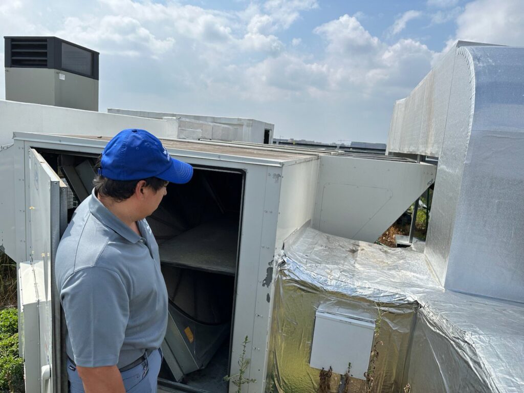 A technician from American Air LLC inspecting a large commercial rooftop HVAC unit in Moncks Corner, SC