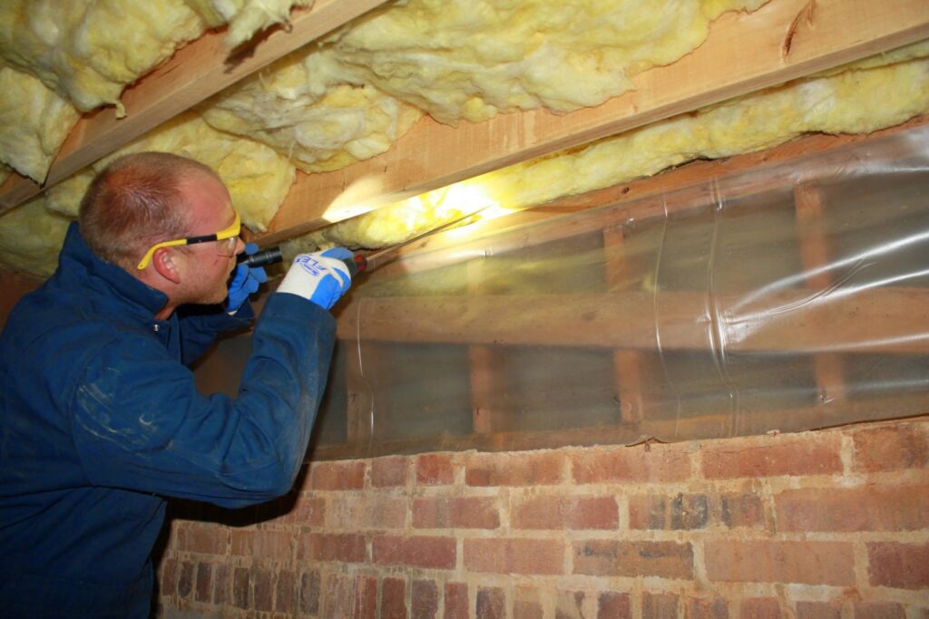 A Capital Pest Services technician inspecting a crawl space for pests with a flashlight in Raleigh, NC.