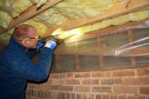 A Capital Pest Services technician inspecting a crawl space for pests with a flashlight in Raleigh, NC.