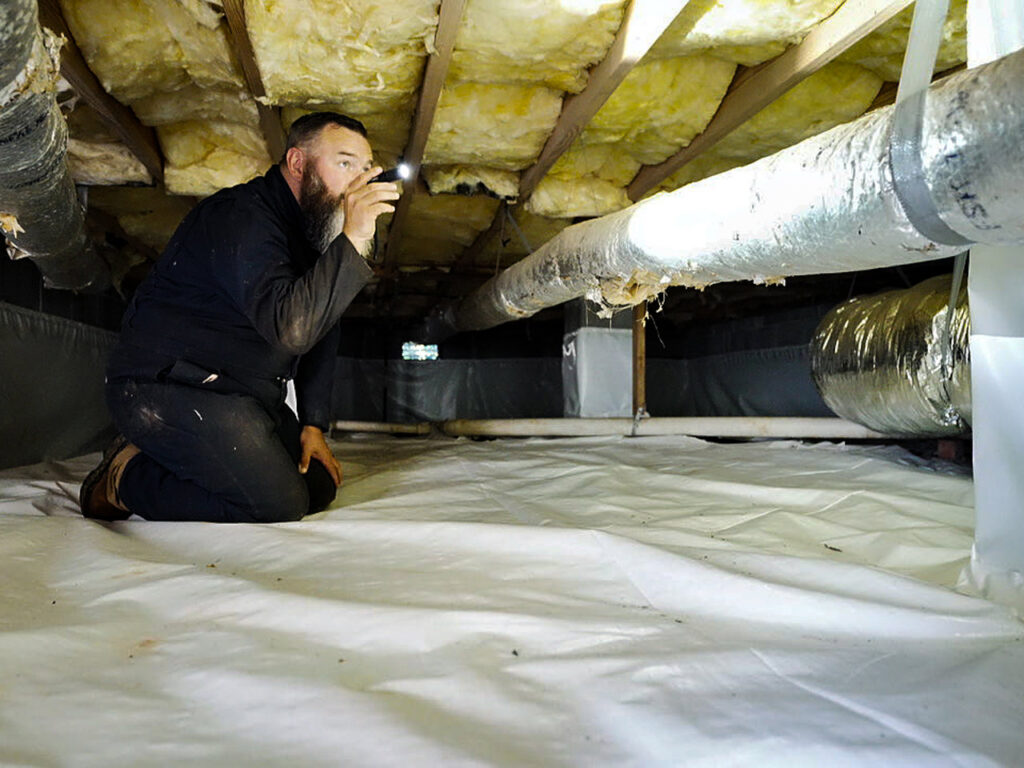 A Pest Magic Pest Control technician inspecting a crawl space with a flashlight for pests in Forsyth, GA.