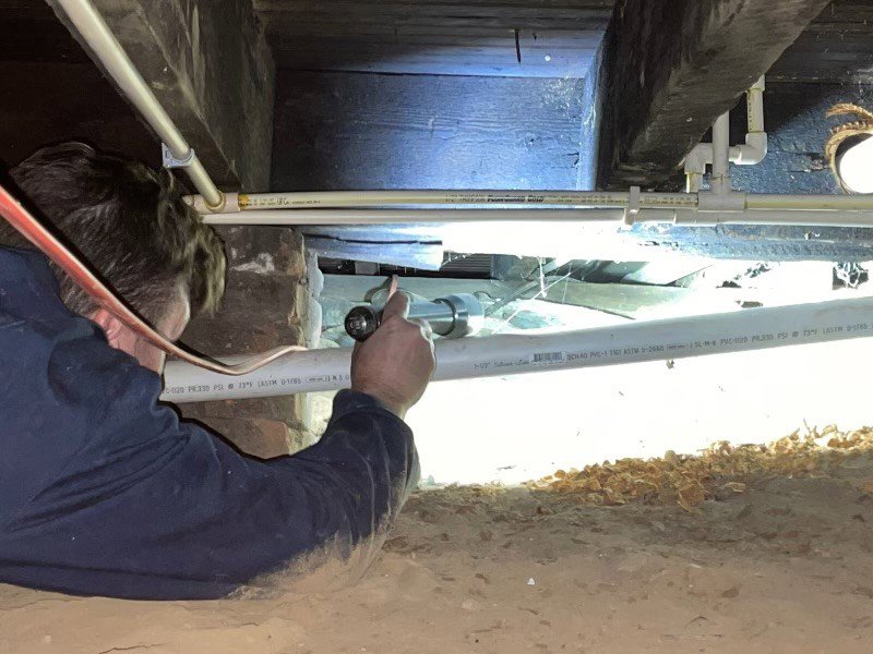 A PestNation technician inspecting a dark crawl space with a flashlight for pests in Buford, GA
