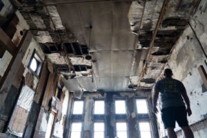A pest control technician inspecting a severely damaged building, likely for pest or wildlife damage assessment, for Complete Pest Solutions of Canton in North Canton, OH.