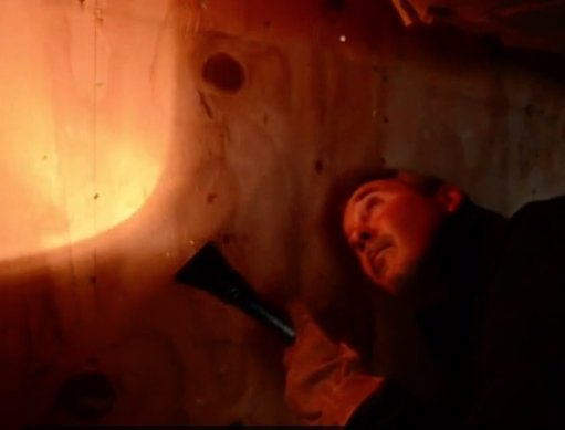 A technician from Omega Termite and Pest Control in Oakland, CA, using a flashlight to inspect a dark area for pest activity.