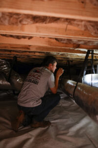 A technician inspecting ductwork in a crawl space or tight area with a flashlight for Grace Heating & Air in Clarksville, TN.