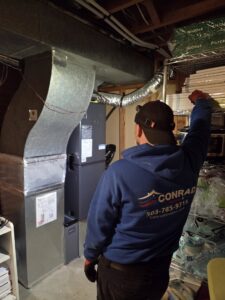 A Conrad Heating and Cooling technician inspecting ductwork and a furnace in Beaverton, OR.