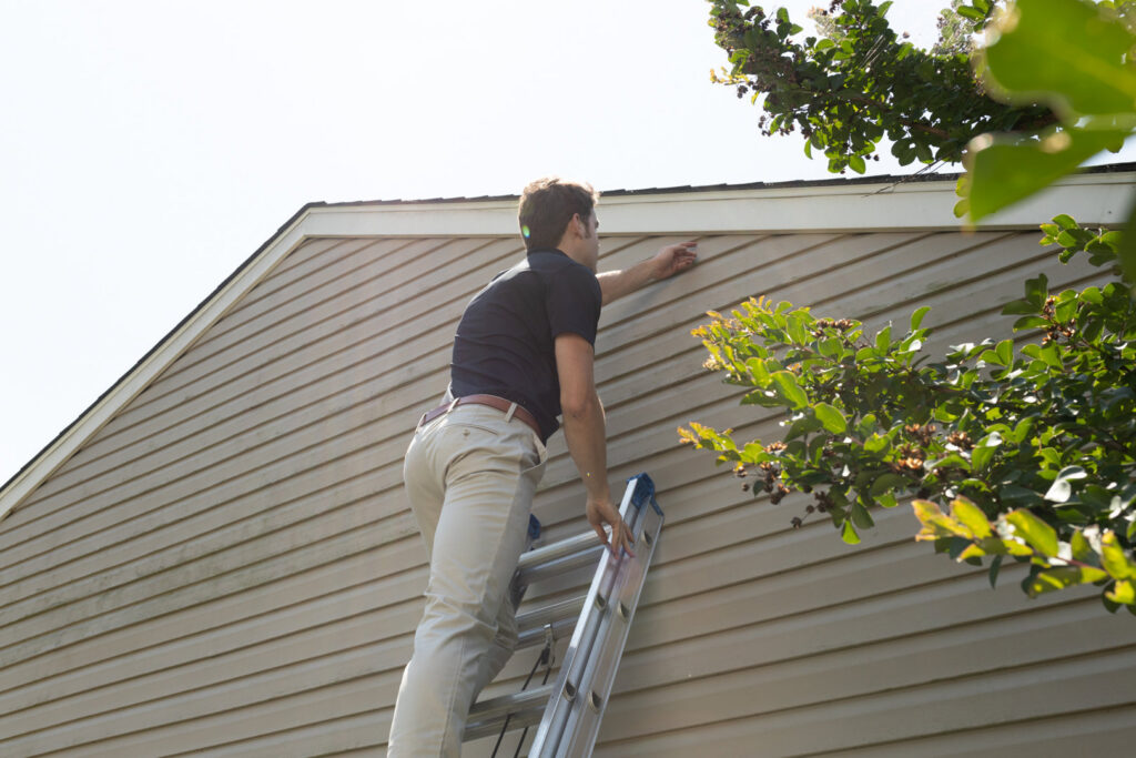 A Critter Control of Charleston, SC technician on a ladder inspecting the eaves of a house for wildlife entry points.