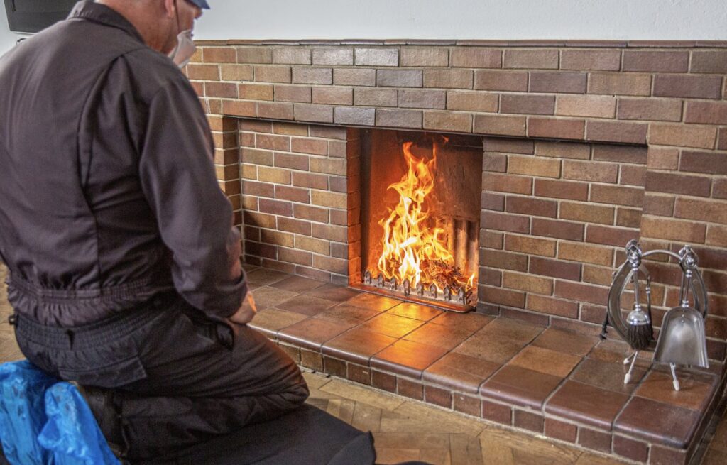 A technician from Top Chimney Fix inspecting a brick fireplace with a fire burning in Denver, CO.