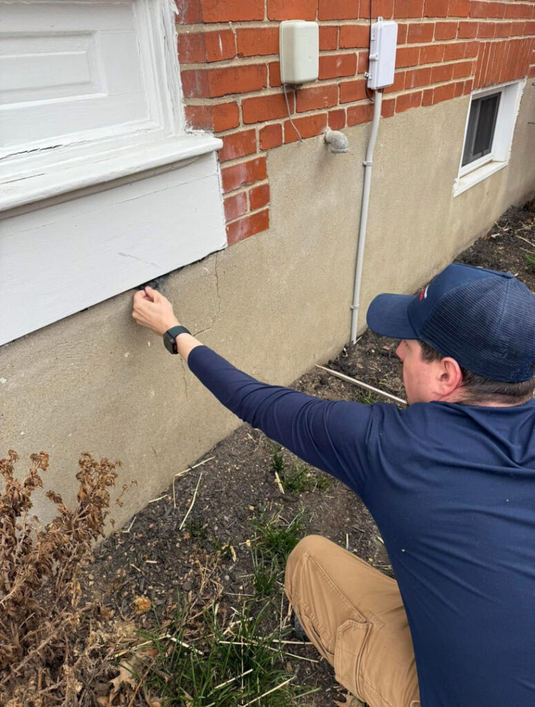 A pest control technician inspecting a crack in a building's foundation for pest entry points at Devlins Pest Control in Reading, PA.
