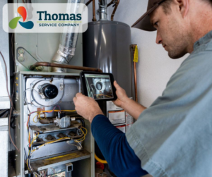 A technician inspecting a furnace or HVAC unit with a tablet for Thomas Service Company in Huntsville, AL