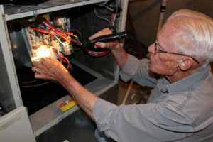 A technician inspecting the internal wiring of a furnace with a flashlight for West Wichita Heating & Air Conditioning in Wichita, KS.