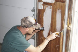 A pest control technician inspecting a wooden garage door frame with a flashlight for signs of pests or damage by Midwest Pest Control in East Peoria, IL.