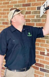 A Sustainable Pest Systems technician inspecting a house exterior for pests with a flashlight in Raleigh, NC.
