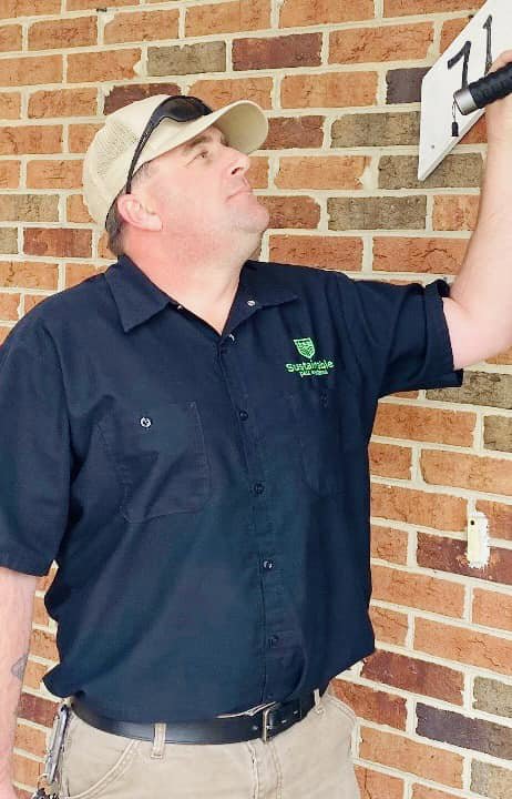 A Sustainable Pest Systems technician inspecting a house exterior for pests with a flashlight in Raleigh, NC.
