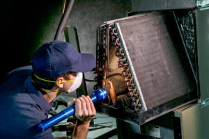 A DUCTZ of Siouxland technician inspecting an HVAC coil unit with a flashlight as part of a service job in Vermillion, SD.