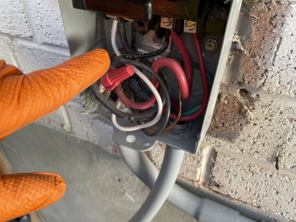 A technician's gloved hand pointing at electrical wiring inside an HVAC disconnect box during service by LUCAS Heating And Air LLC in Salt Lake City, UT.