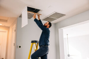 A technician from Rusty's Air Conditioning And Heating inspecting an indoor air vent or return on a ladder in Mesa, AZ.