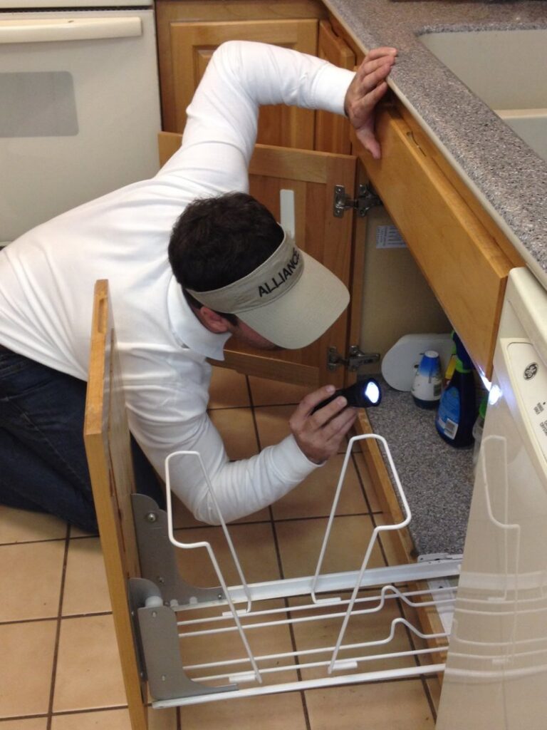 A technician from Alliance Pest Control inspecting under a kitchen sink cabinet with a flashlight in Alliance, OH