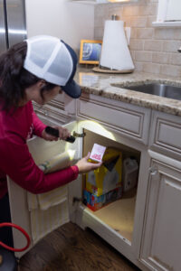 A Pest Authority Des Moines technician inspecting under a kitchen cabinet with a flashlight in Des Moines, IA.