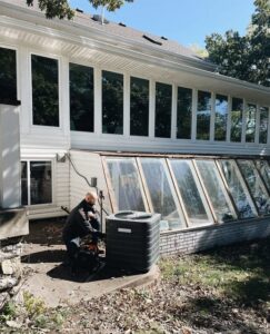 A technician from Davis Heating, Air Conditioning & Home inspecting an outdoor AC unit at a residential property in Overland Park, KS.