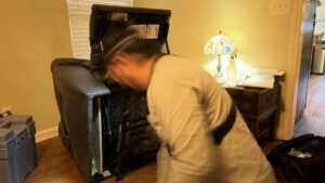 A pest control technician inspecting the underside of a recliner chair for pests at Tailor Made Pest and Wildlife in Louisville, KY.
