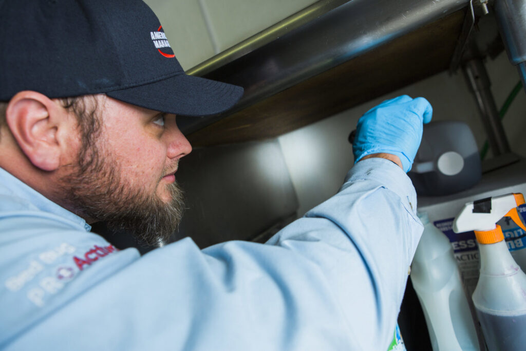 A pest control technician inspecting an area under a shelf for signs of pests for American Pest Management in Saint Petersburg, FL.