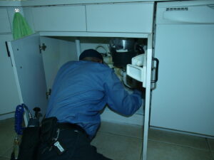 A Shield Pest Control technician inspecting or treating under a kitchen sink for pests in Homestead, FL.