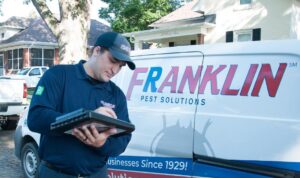 A Franklin Pest Solutions technician inspecting and writing on a clipboard next to a company van in Lafayette, IN.