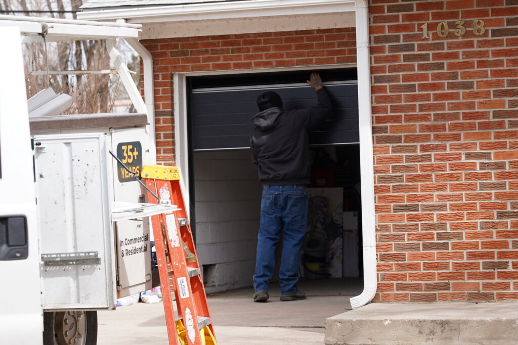 A Prutch's Garage Door technician installing a new black garage door on a brick residential home in Colorado Springs, CO
