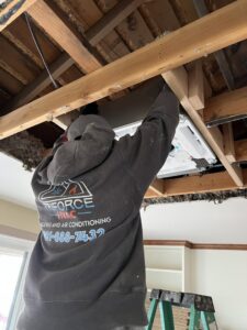 A TriForce HVAC technician installing a ceiling cassette unit into a framed opening in a ceiling in Layton, UT