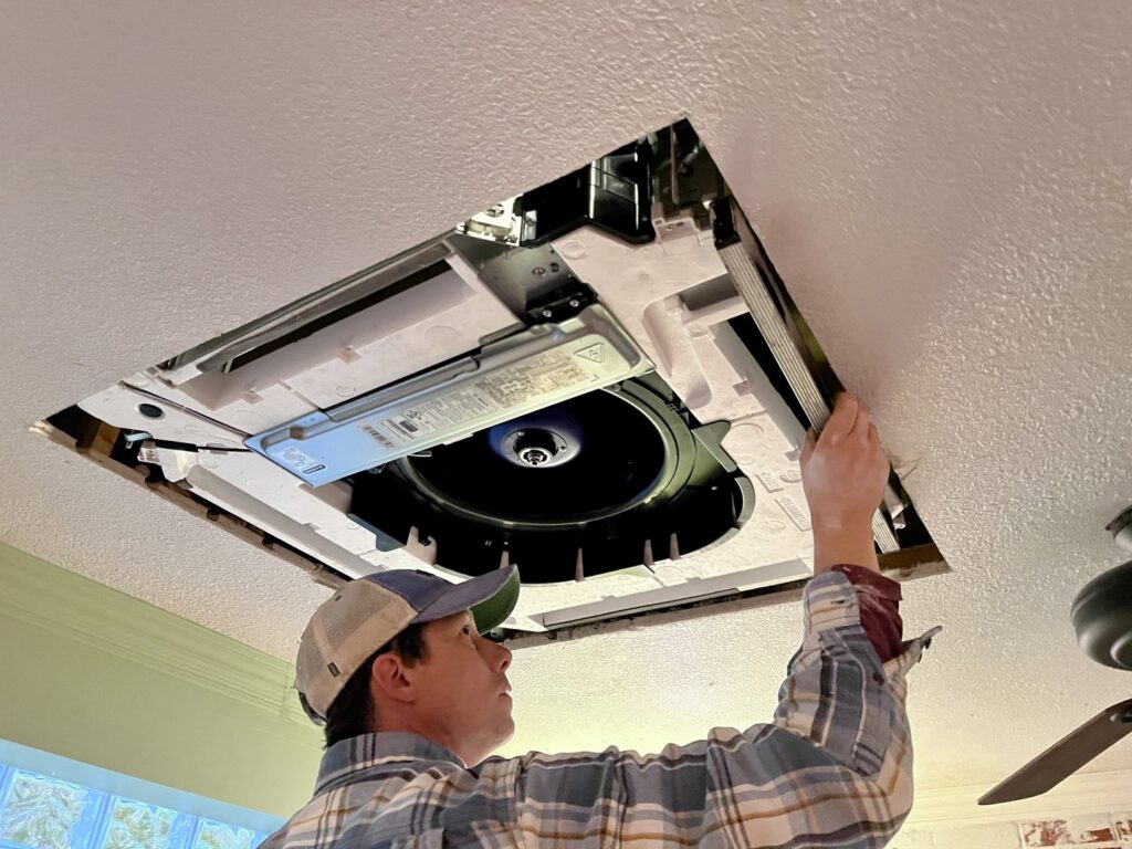 A Just Heat Pumps technician installs a ceiling-mounted HVAC unit in a residential property in Denver, CO.