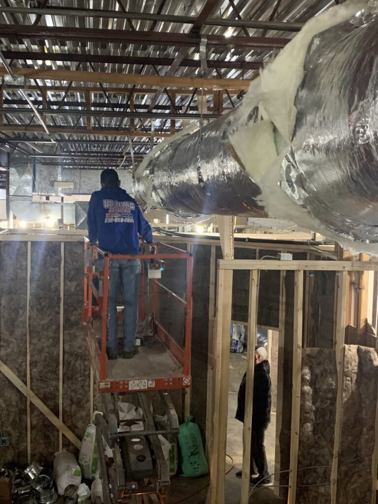 A U.S. HVAC Services technician installing large commercial ductwork from a lift in Madison, AL.