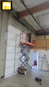 Technician installing a large commercial garage door from a scissor lift for TH Locksmith And Garage Door Repair, Vancouver, WA.