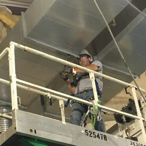 A Crome Mechanical Inc. technician installing large commercial ductwork from a scissor lift in Cedar Springs, MI