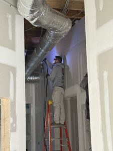 An Infinite Comfort technician installing new ductwork on a ladder in Youngsville, NC.