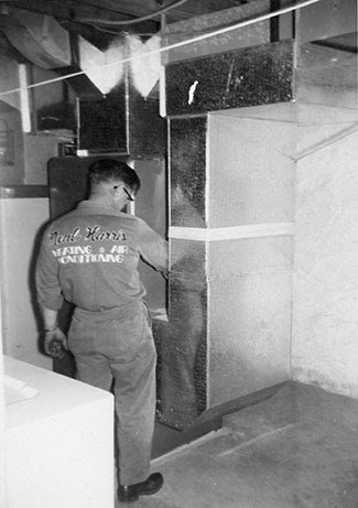 A technician from Neal Harris Service Experts installing or servicing ductwork in a basement in Overland Park, KS.