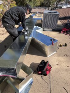 A technician from Arizaz Heating & Cooling installing new ductwork on a rooftop next to an AC unit in Chandler, AZ.