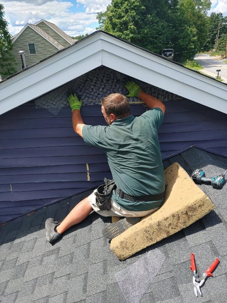 A technician installing exclusion mesh on a gable vent to prevent wildlife entry for New England Wildlife Control in Salem, NH.