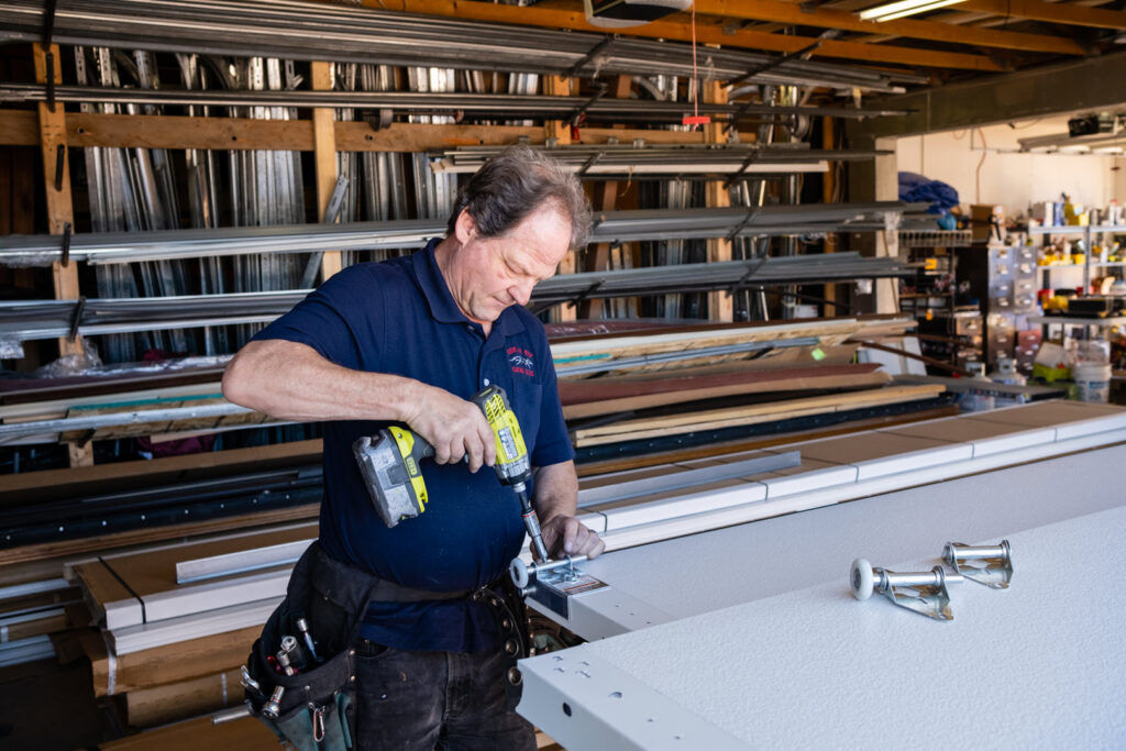 A garage door technician using a drill to install hardware onto a new garage door panel for Above The Rest Garage Door in Colorado Springs, CO.