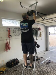 A Team Garage Doors technician on a ladder installing a garage door opener in Mesa, AZ.