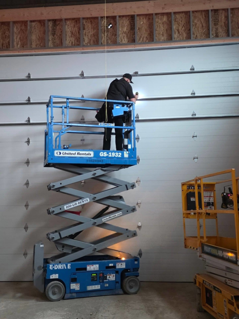 A technician on a scissor lift installing upper garage door panels for Iconic Garage Door Service in Queen Creek, AZ
