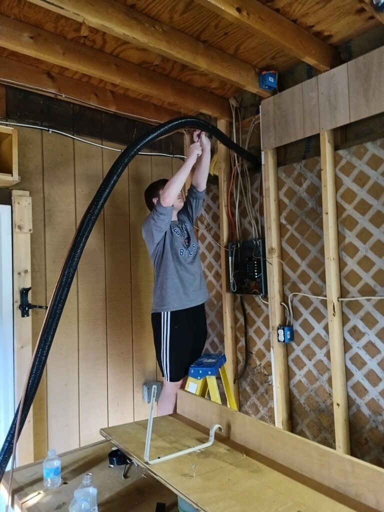A TAS Mechanical Services technician installing flexible HVAC ductwork or wiring in a residential space in Kearney, MO.
