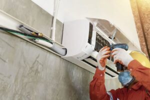 A technician installing or repairing an indoor mini-split AC unit with a drill for Ault's Cooling HVAC Services LLC in Chandler, AZ.