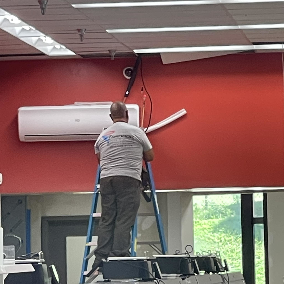A Tornado Heating and Air technician on a ladder installing a mini-split AC unit in Tulsa, OK.