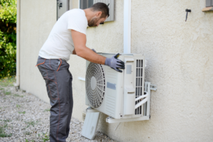 A technician installing or adjusting an outdoor mini-split air conditioning unit on a wall for Custom Heating & Air Conditioning - Nampa in Nampa, ID.
