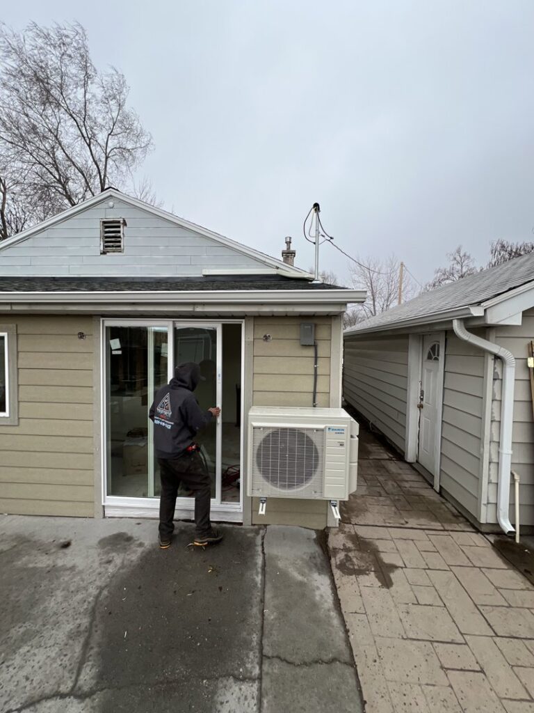 A TriForce HVAC technician installing an outdoor mini-split air conditioning unit on the side of a building in Layton, UT