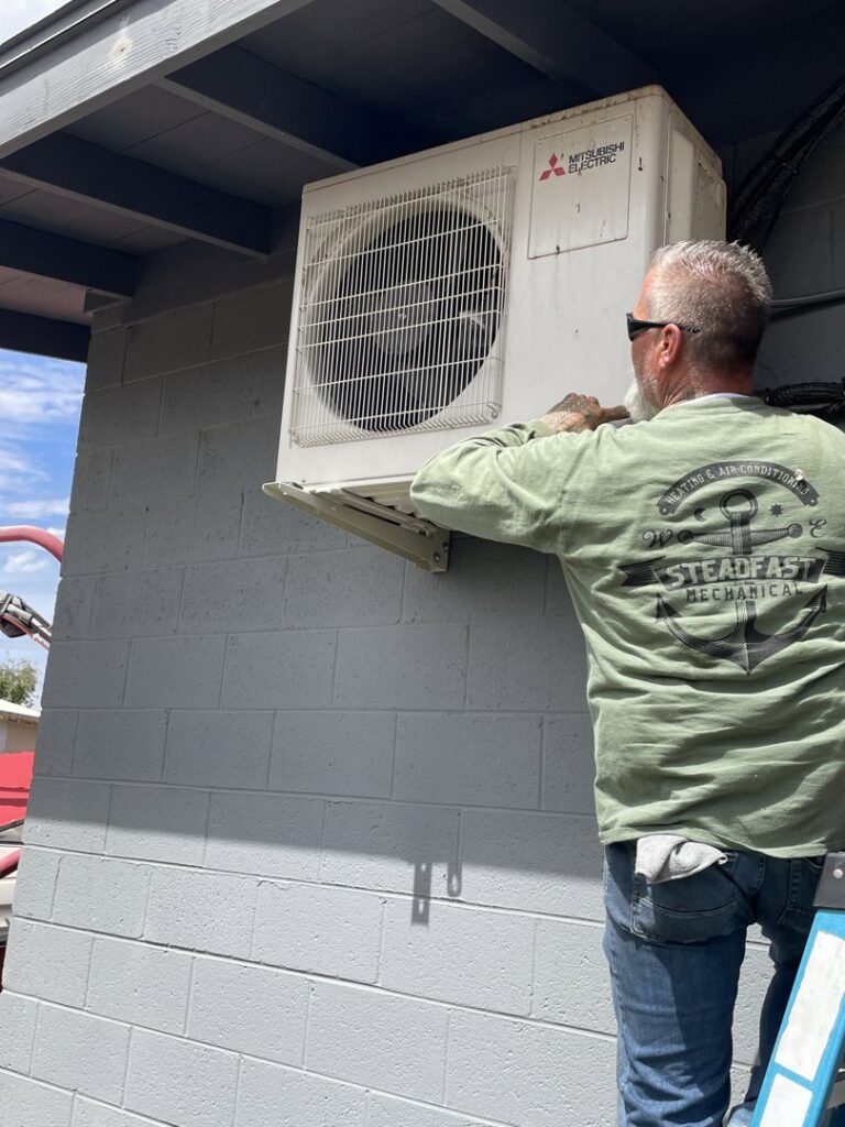A Steadfast Mechanical technician installing a wall-mounted mini-split outdoor unit in Gilbert, AZ.