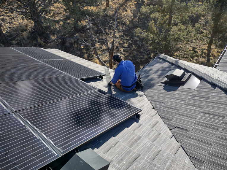 A Solid Pest Solutions technician installing pest exclusion mesh under solar panels on a roof in Bend, OR.